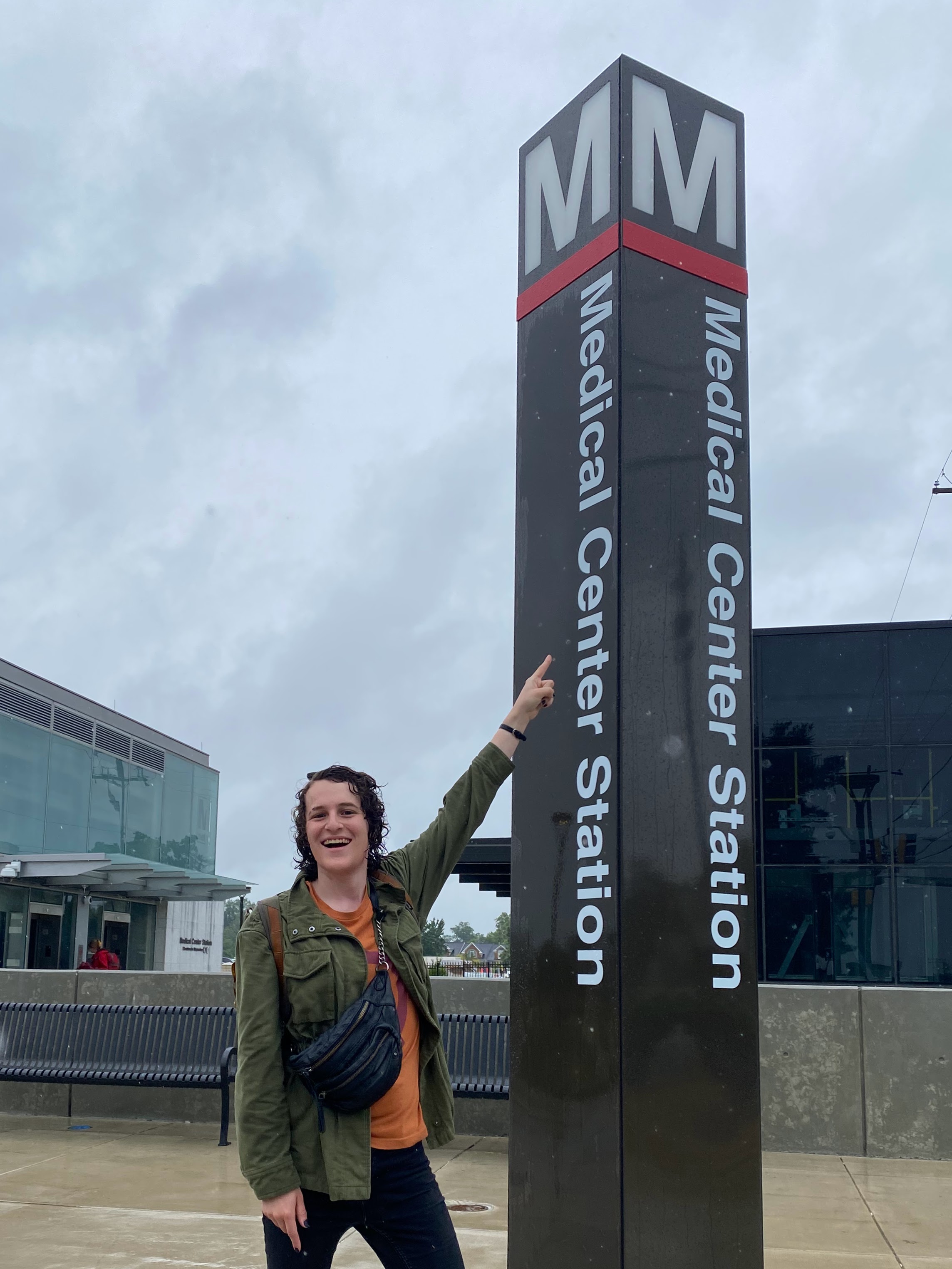 Emily pointing at the sign marking the entrance to the DC Metro's Medical Center station.